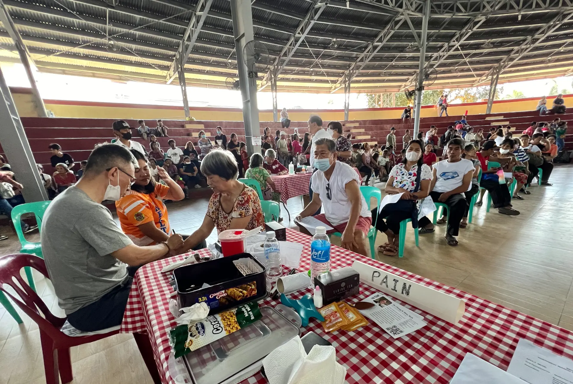 Dr. Shin examining a patient at a community medical mission clinic in the Philippines, with people waiting nearby